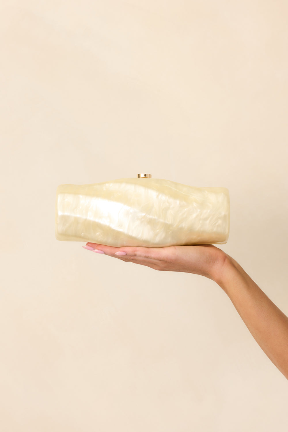 champagne-pearlescent-spiral-clutch-held-front-beige-background